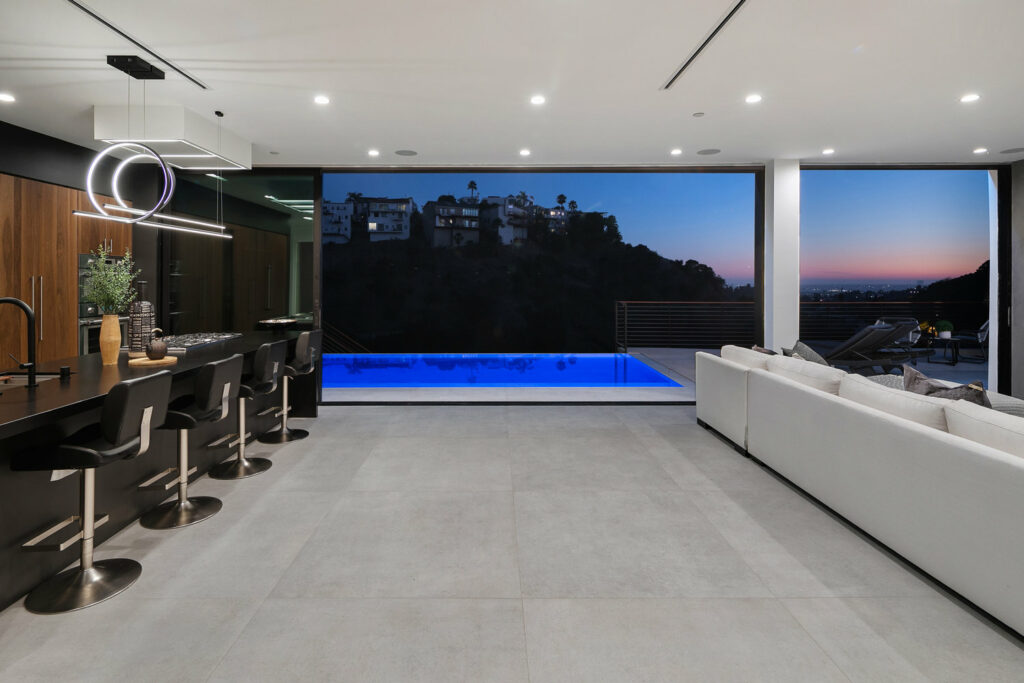 Modern kitchen opening to poolside at dusk.