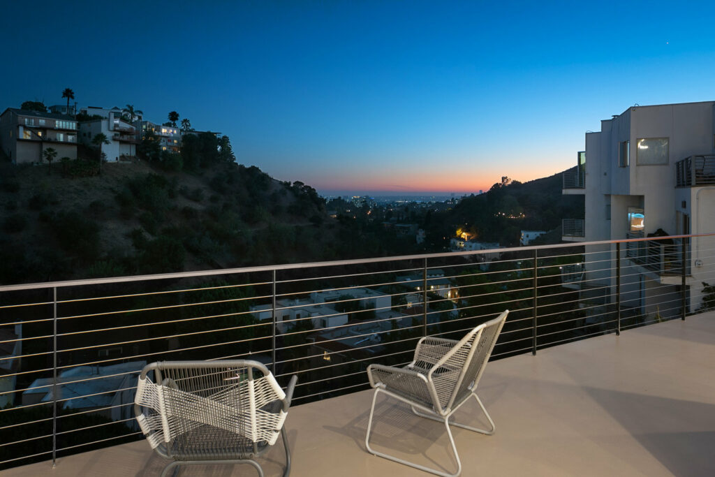 Balcony view of sunset over hills with outdoor chairs.