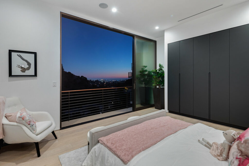Modern bedroom with city view at dusk.