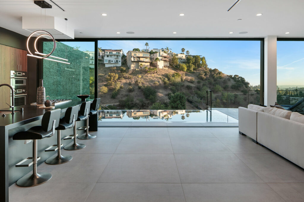 Modern kitchen overlooking hills through large glass windows.