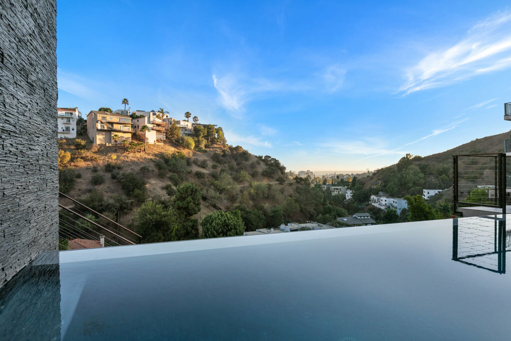 Infinity pool overlooking hillside homes at sunset.