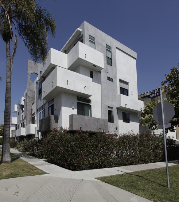 Modern apartment building with palm trees under blue sky.