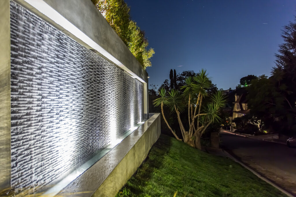 Illuminated waterfall feature at night with starry sky.