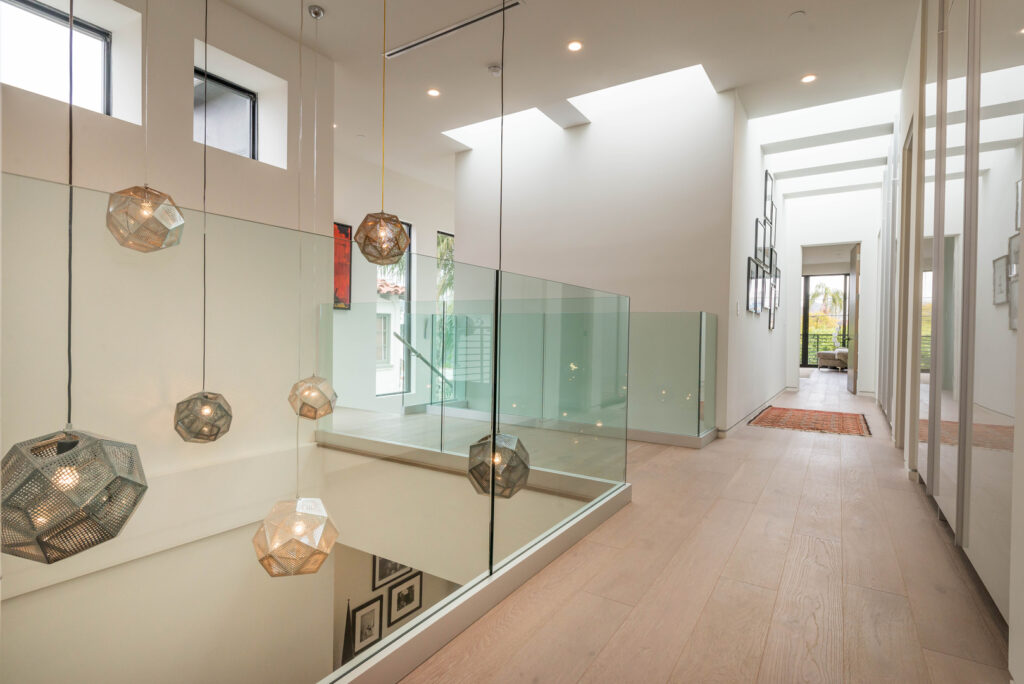 Modern hallway with geometric pendant lights and glass balustrade.