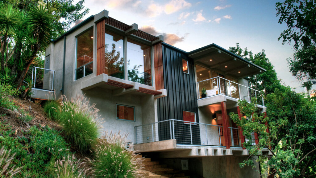 Modern hillside house with large windows and balconies.