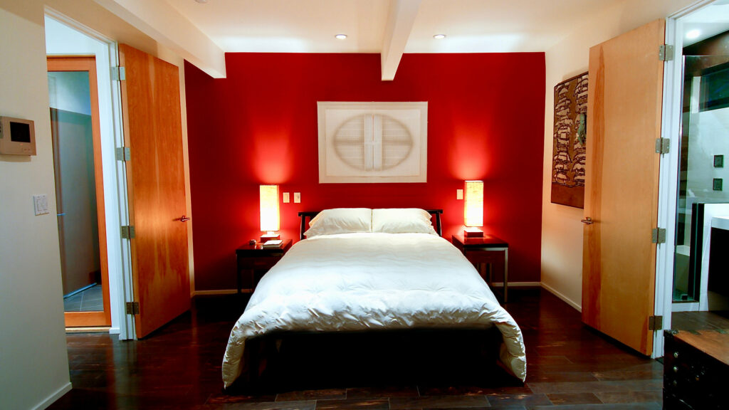Modern bedroom with red walls and white bedding.