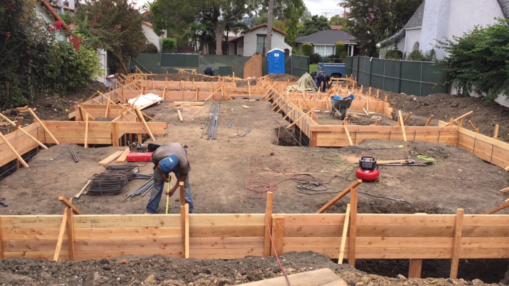 Construction site with workers building wooden foundation forms.
