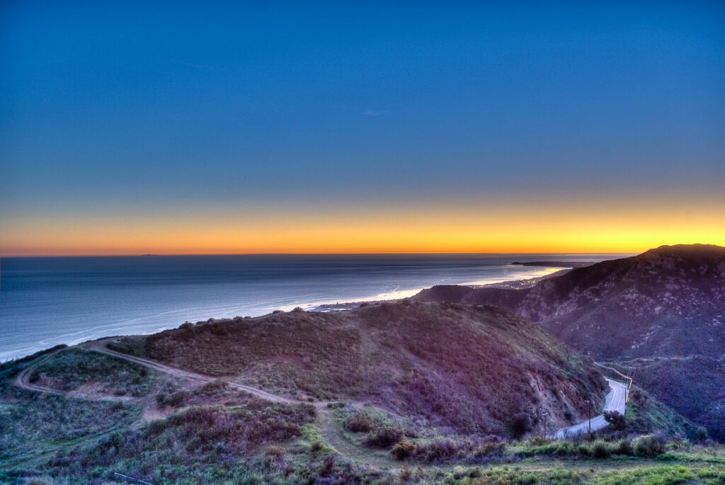 Coastal sunset view with winding trails and hills.