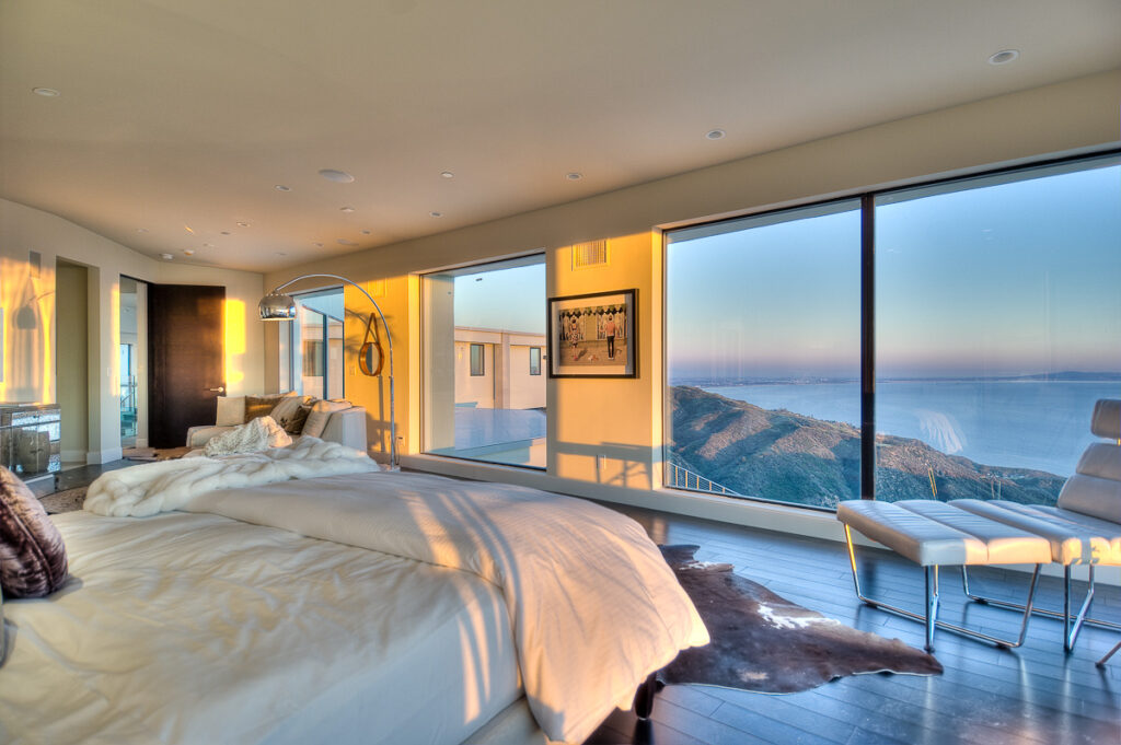 Minimalist bedroom with panoramic ocean view at sunset.