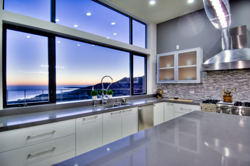 Modern kitchen interior with ocean view at sunset.