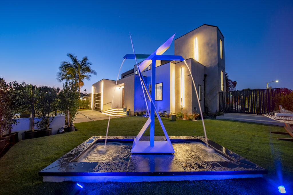 Modern home exterior at dusk with sculpture and fountain.