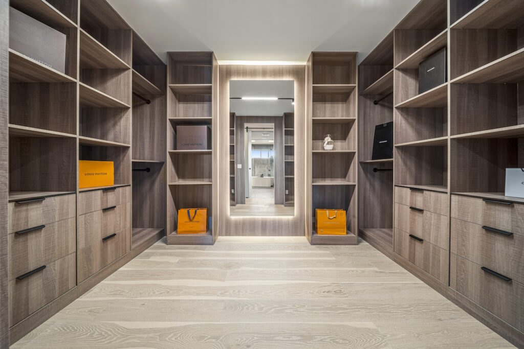 Modern walk-in closet with wooden shelves and lighting.