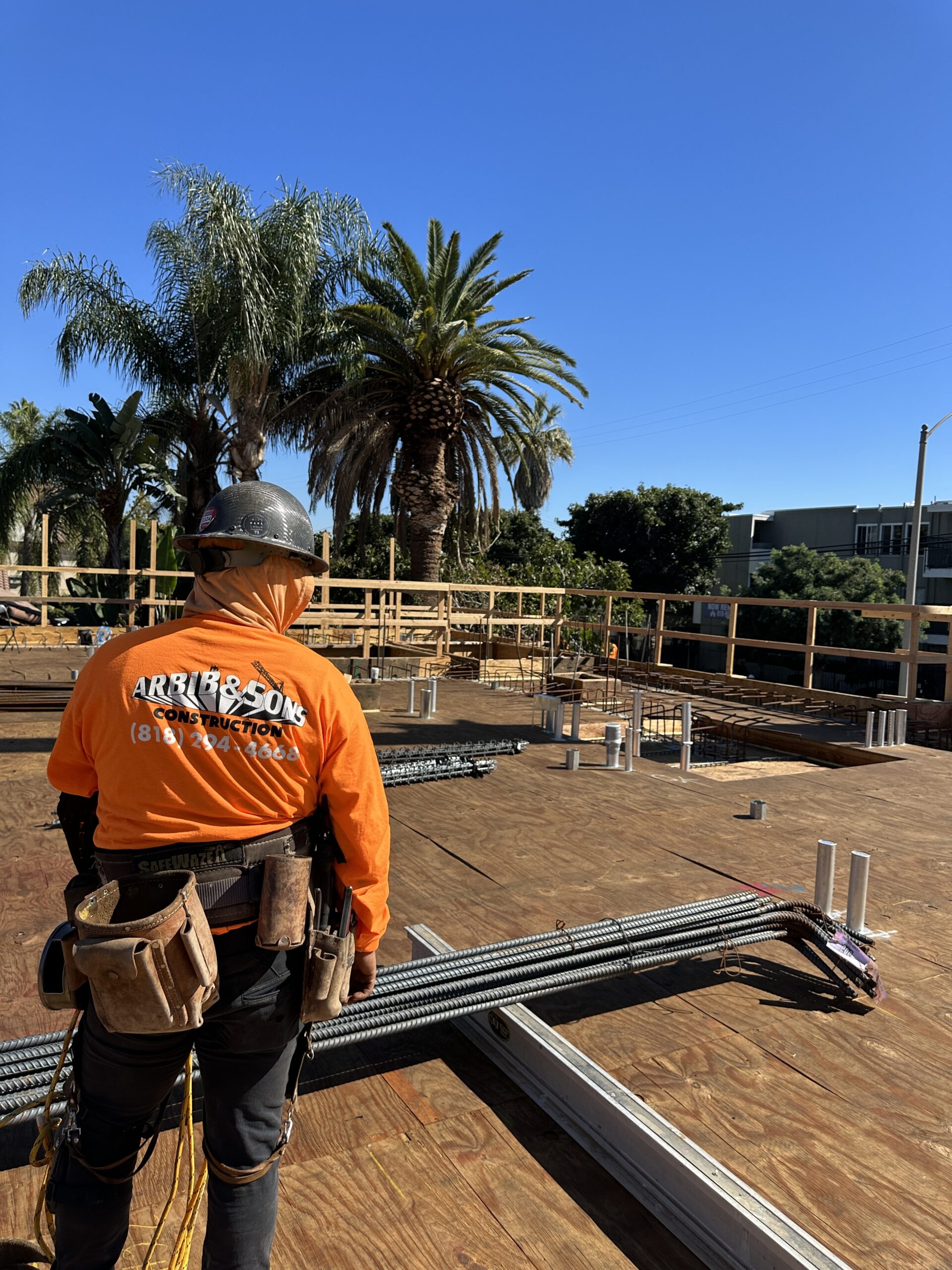 Construction worker overlooking building site with palm trees.