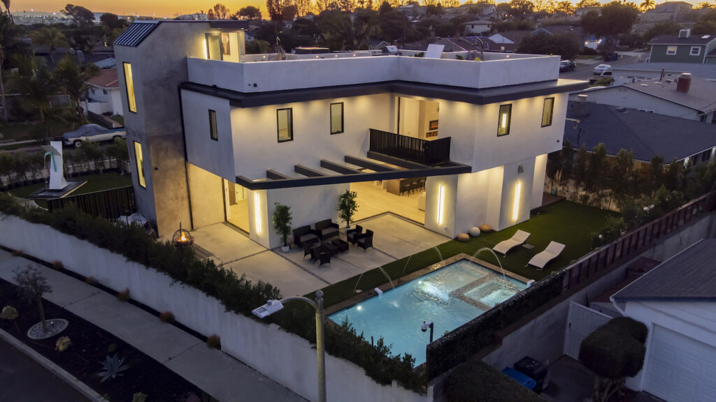 Modern luxury home exterior at dusk with lights and pool.