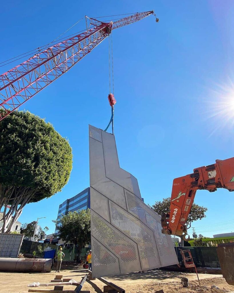 Crane lifting large sculpture outdoor under clear sky.