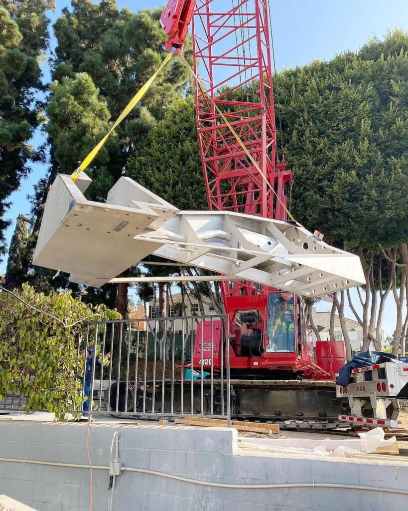 Red crane lifting large structure at construction site.