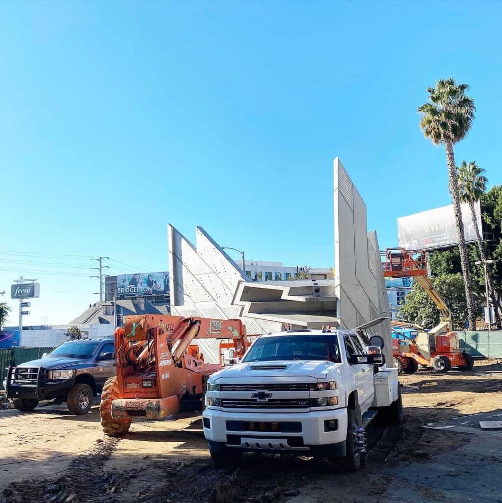 Construction vehicles at urban building site with palm trees.