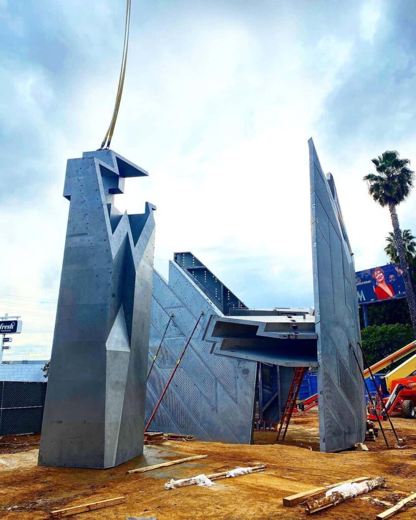 Modern sculpture construction with industrial materials and palm trees.
