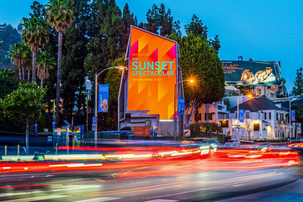 Sunset Boulevard with colorful billboards and streaking car lights.