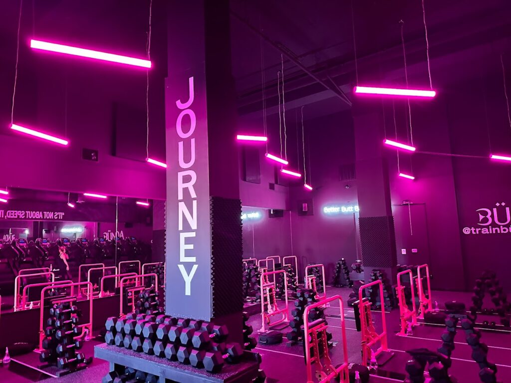 Neon-lit gym interior with weights and "JOURNEY" sign.