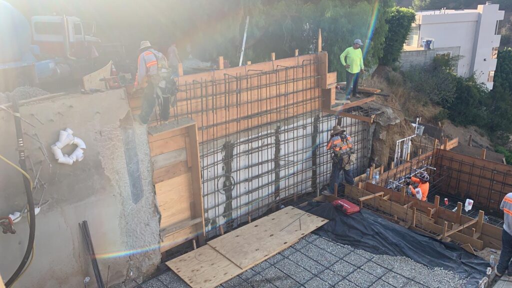 Workers constructing concrete retaining wall at site.