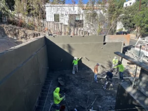 Workers applying concrete to foundation at construction site.