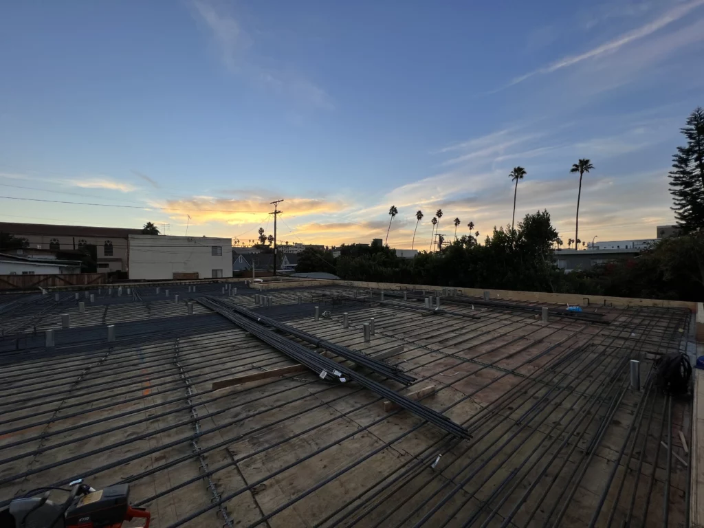 Sunset over urban rooftop construction site with palm trees.