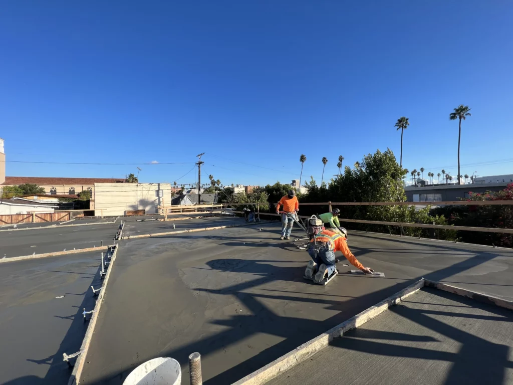 Workers smoothing concrete on rooftop construction site.