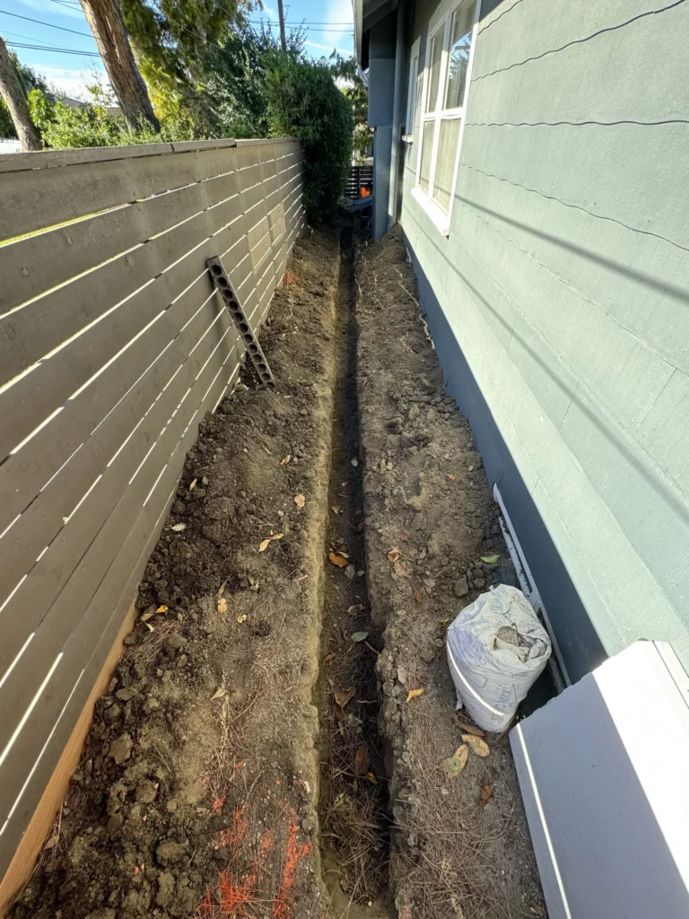Narrow trench along house foundation for repairs.