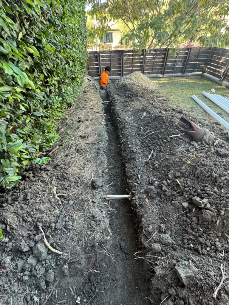 Person inspecting freshly dug trench in backyard.