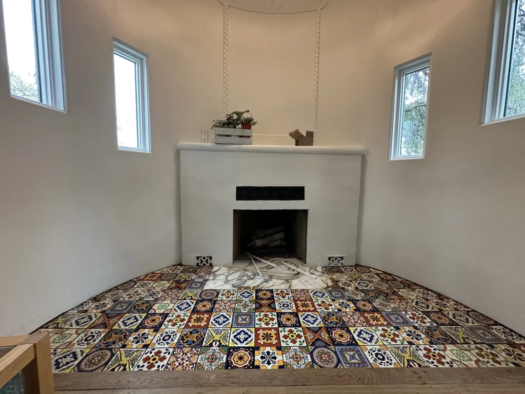 Colorful tiled hearth with white fireplace and windows.