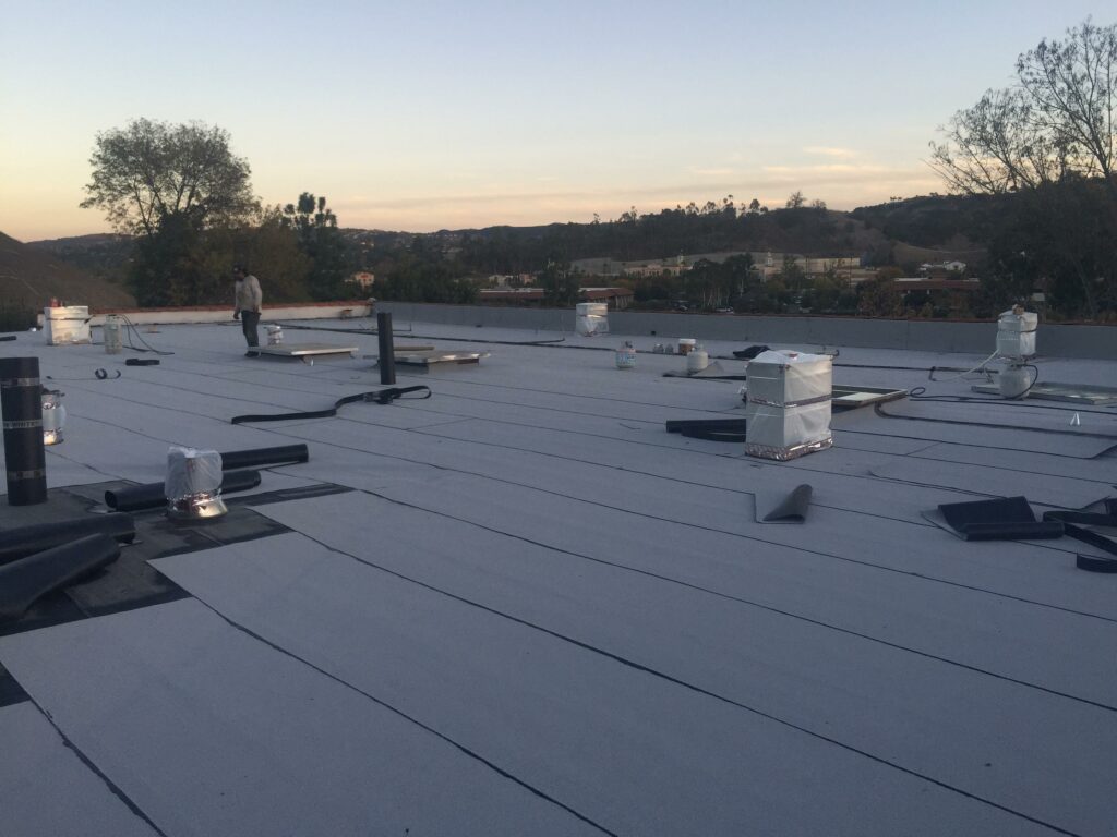Flat roofing installation at dusk with workers and materials.