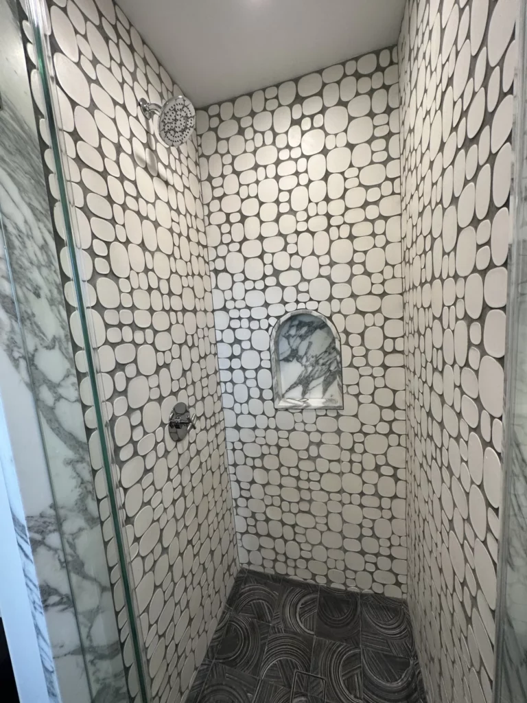 Modern shower with pebble tile and marble walls.