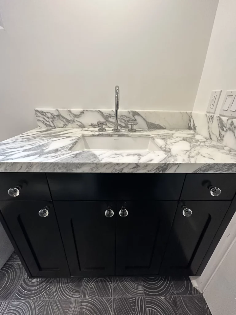 Modern bathroom sink with marble countertop and black cabinets.