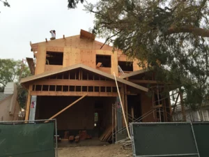 Wooden house construction in progress with worker on roof.