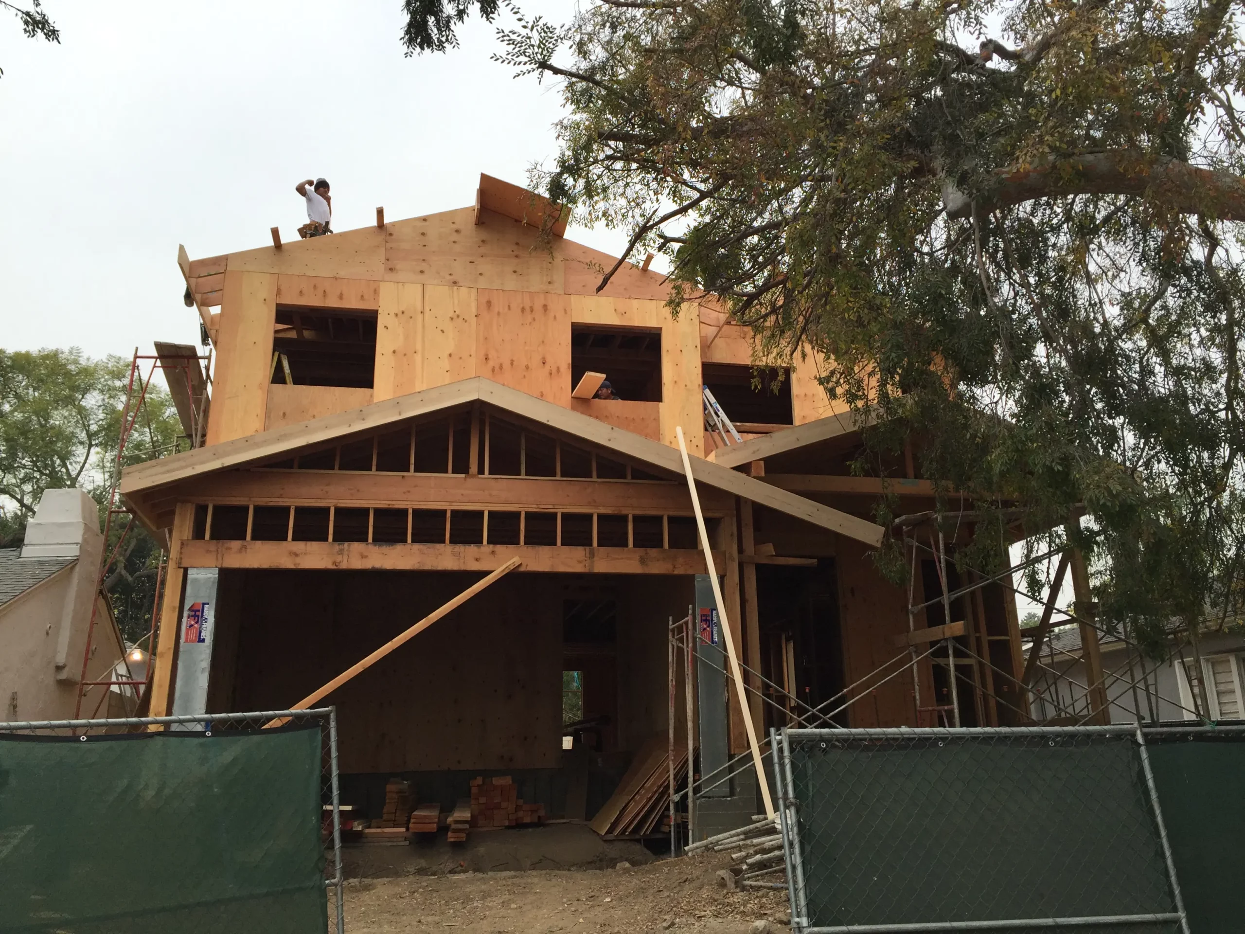 Wooden house construction in progress with worker on roof.