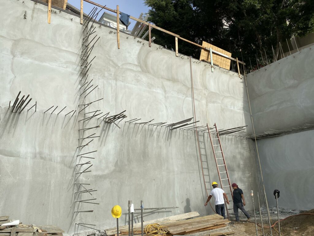 Construction of concrete retaining wall with workers and ladder.