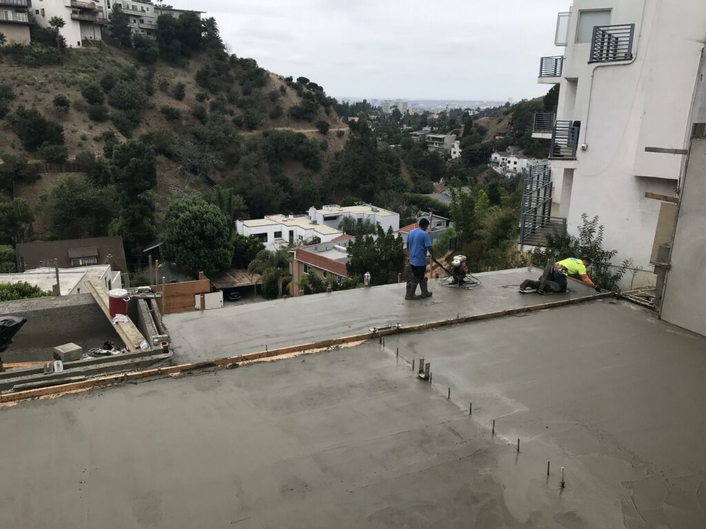 Workers smoothing concrete on rooftop with hillside view.