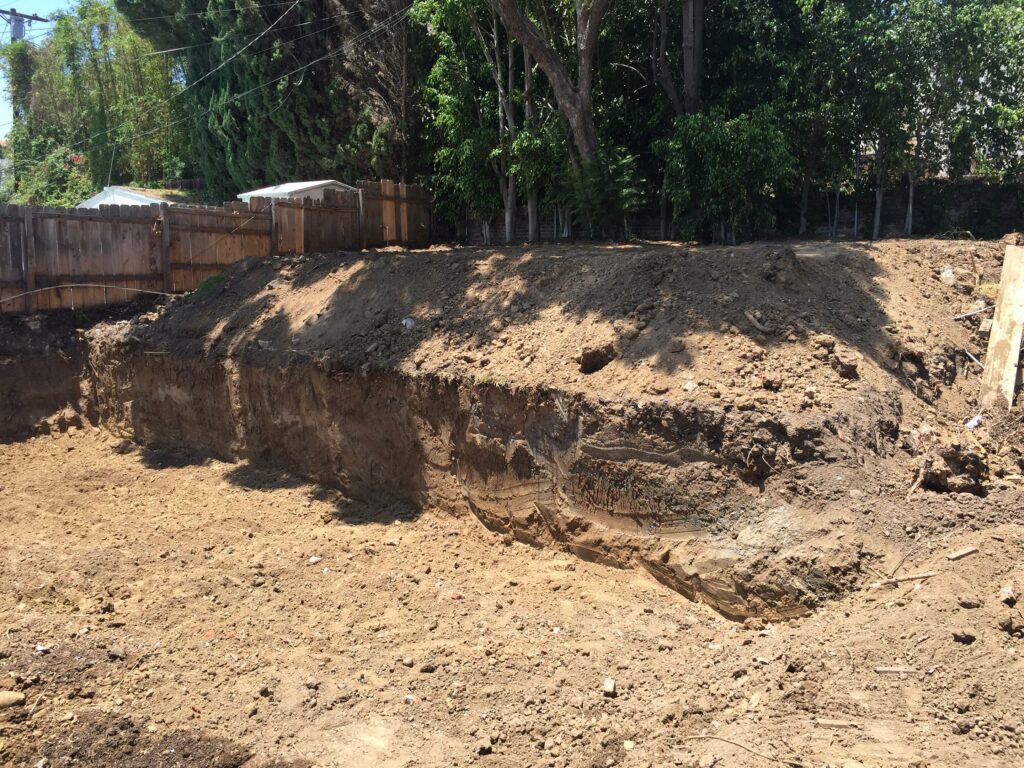 Excavated construction site with exposed soil and trees.