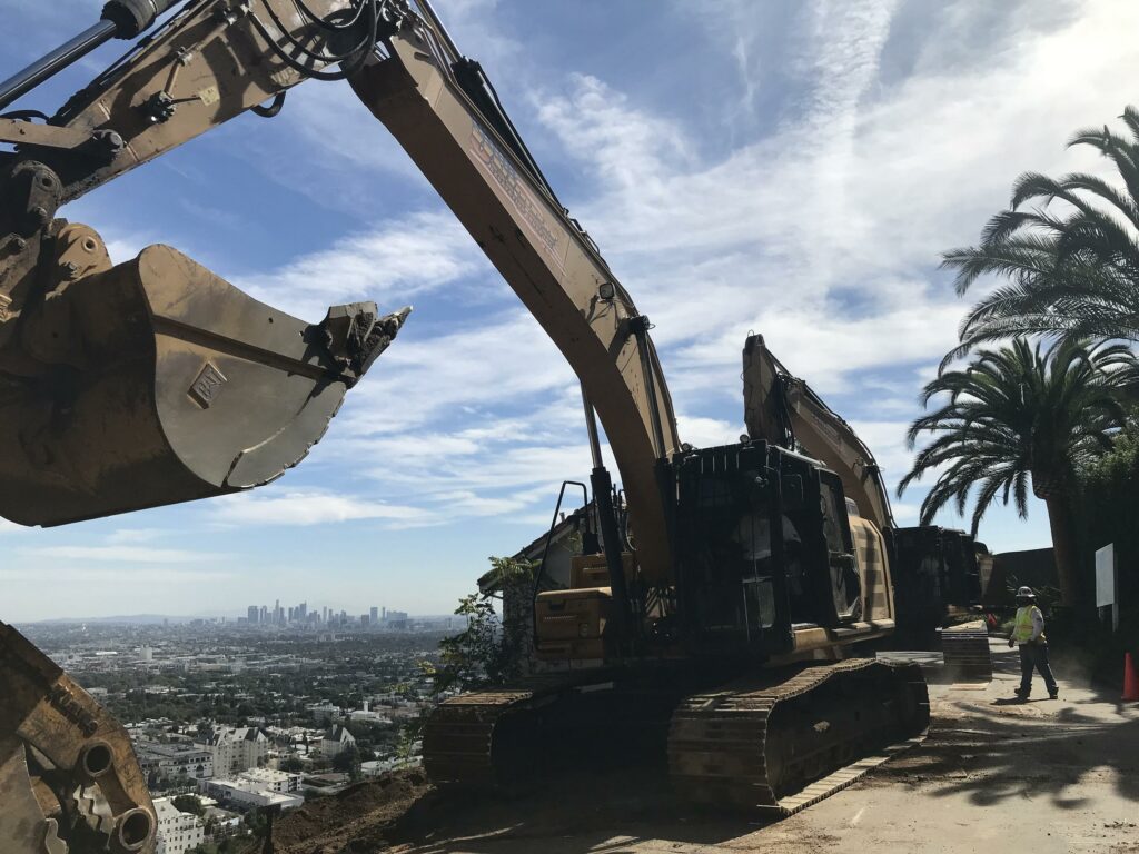 Excavator at construction site with city skyline.
