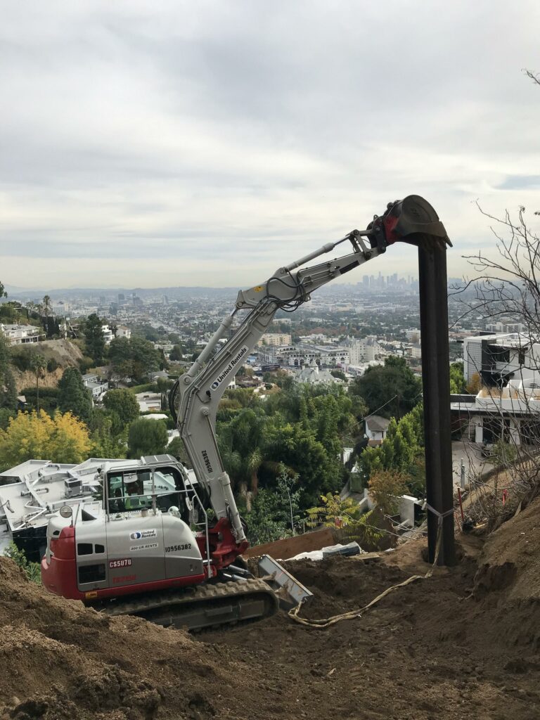 Excavator on a hill with city skyline backdrop.