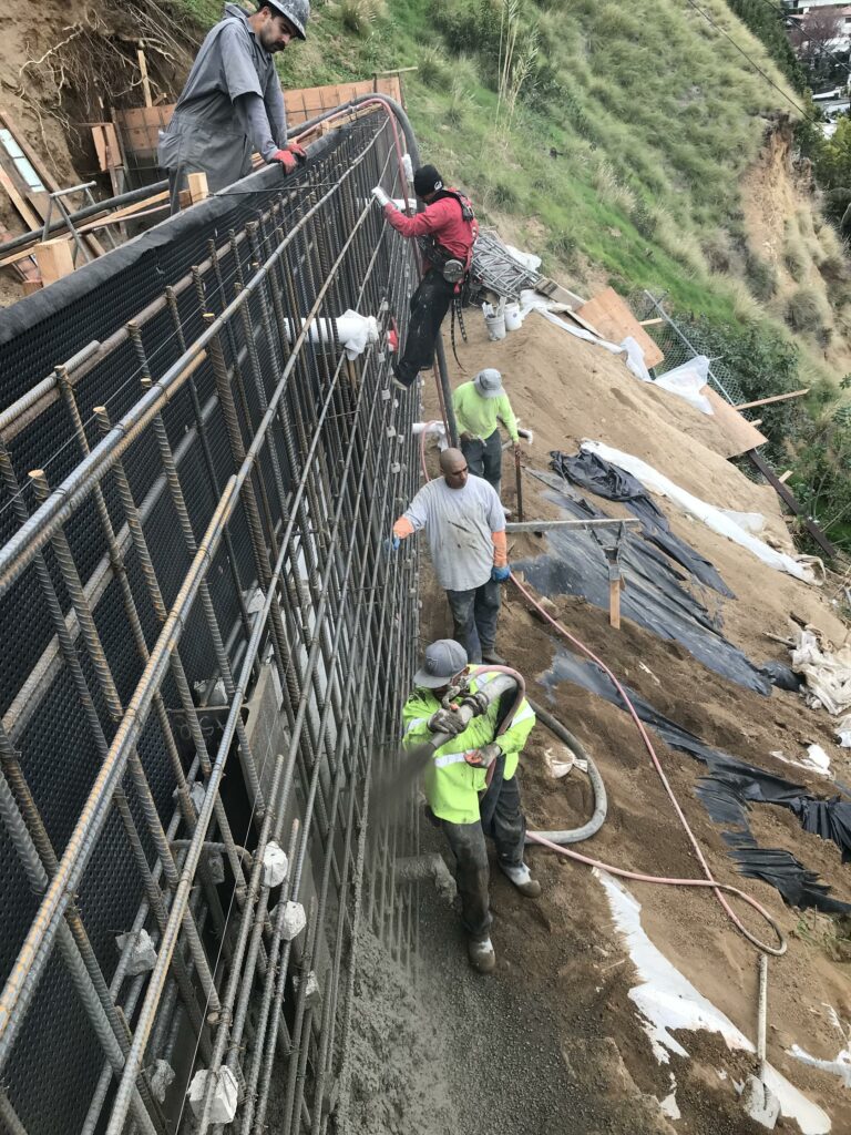 Construction workers pouring concrete on retaining wall.