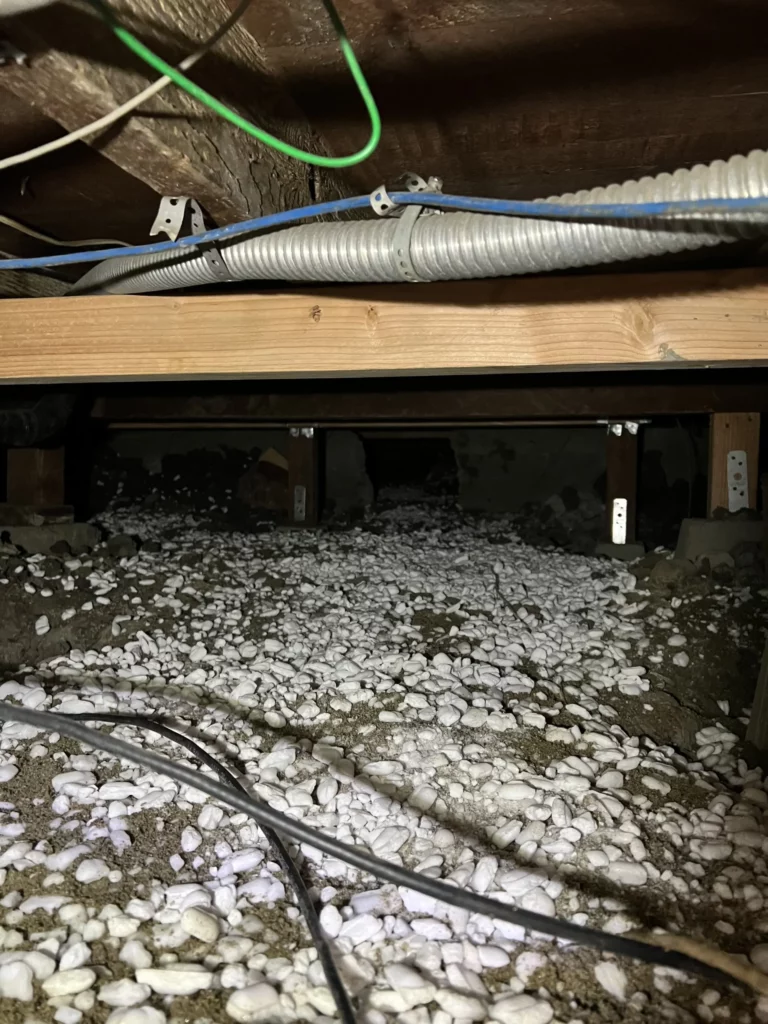 Crawlspace with electrical wiring and white pebble insulation.