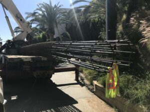 Crane loading rebar cages for construction, safety vest visible.