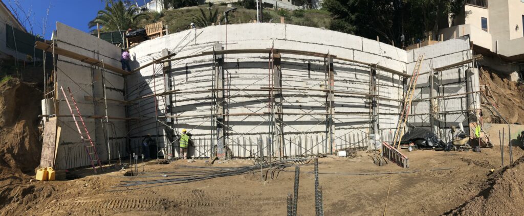 Curved concrete wall construction with scaffolding and workers.