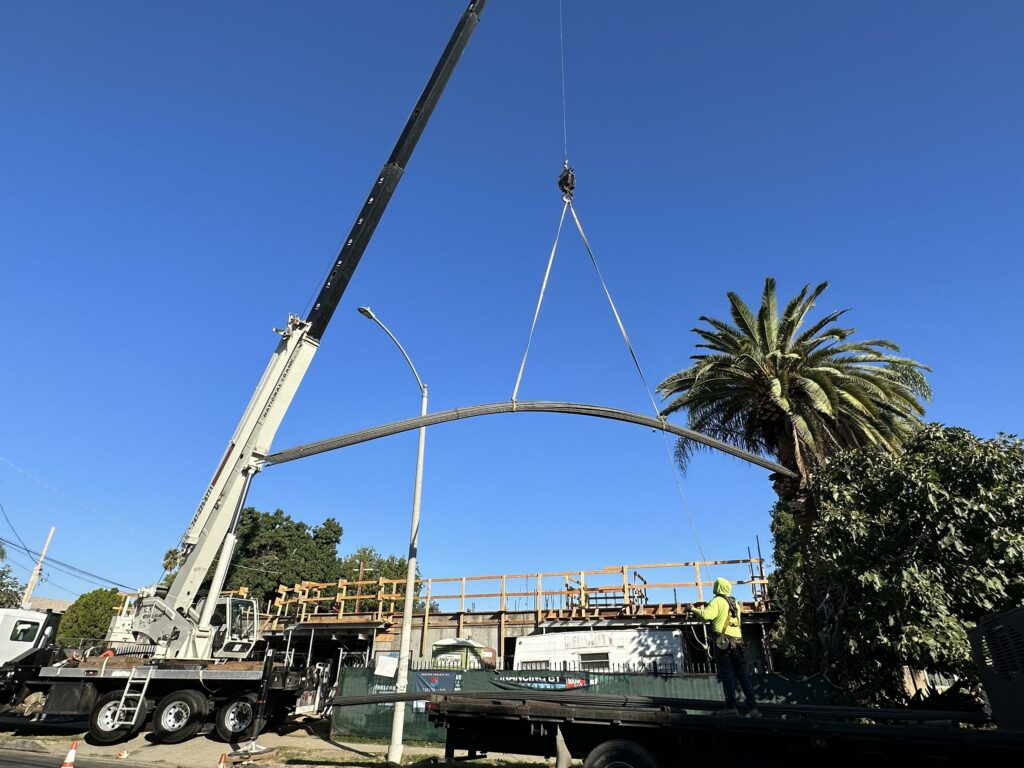Crane lifting steel beam at construction site.