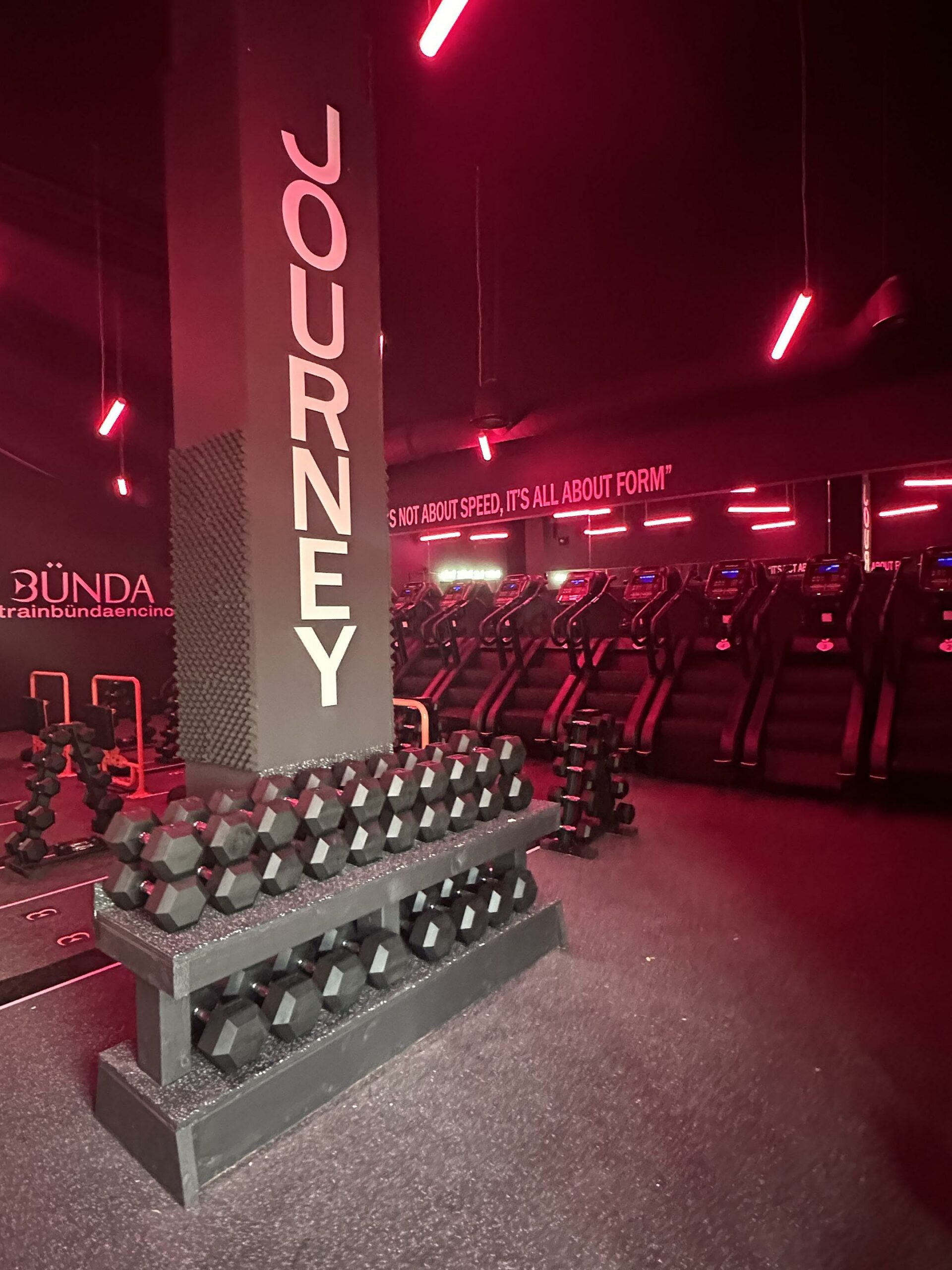 Modern gym interior with red lighting and dumbbell racks.