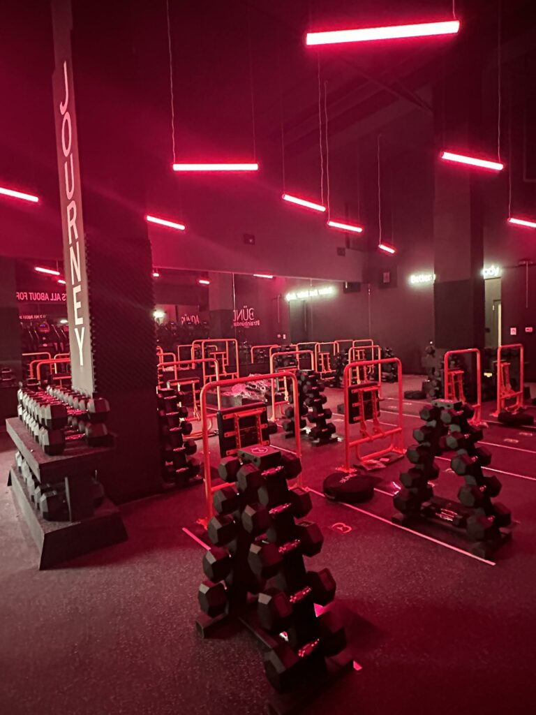 Modern gym with red lighting and weight racks.