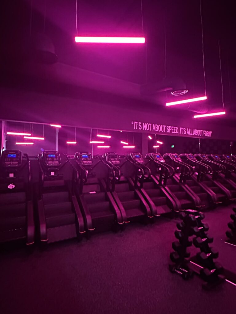 Gym interior with treadmills under pink neon lights