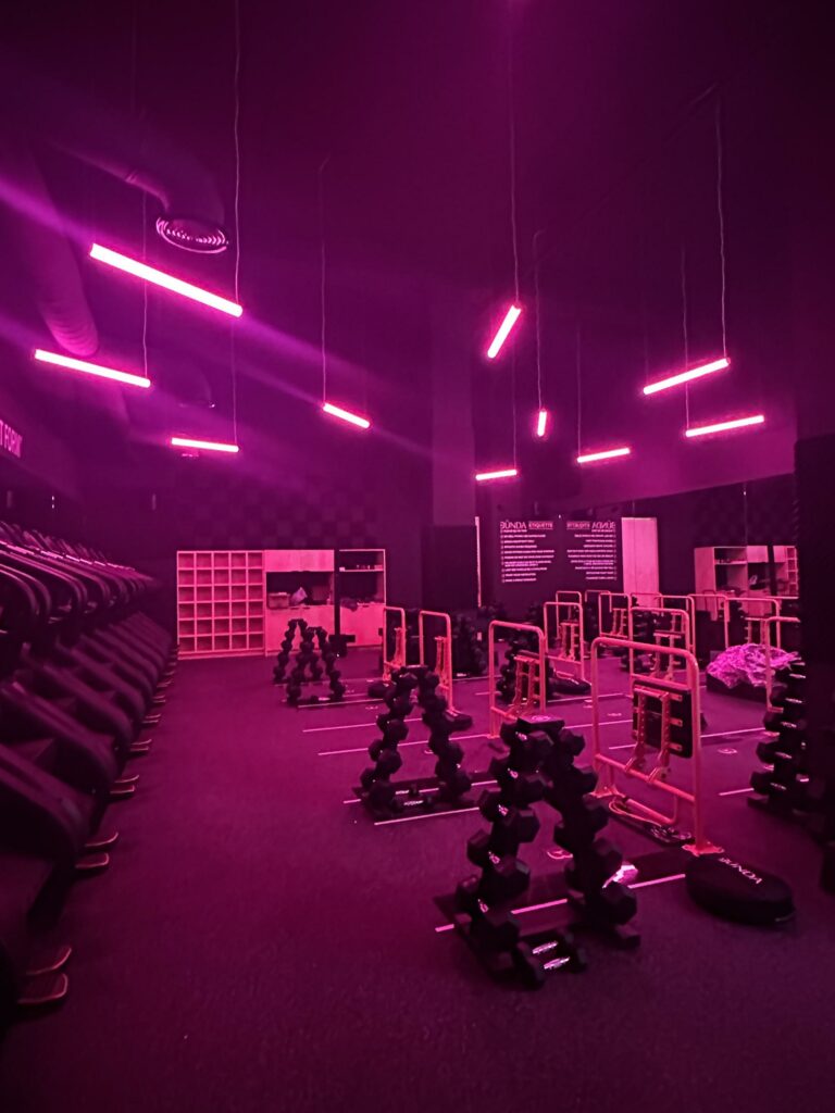 Gym interior with pink neon lights and weightlifting equipment.